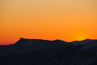 Scenic view of silhouette mountains against orange sky