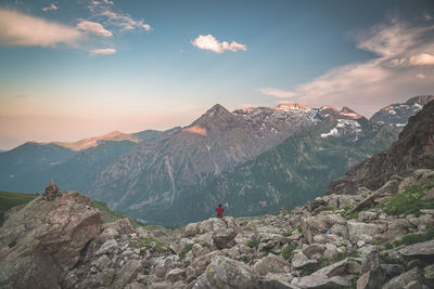 Mid distance view of hiker sitting on rock against mountain range during sunrise