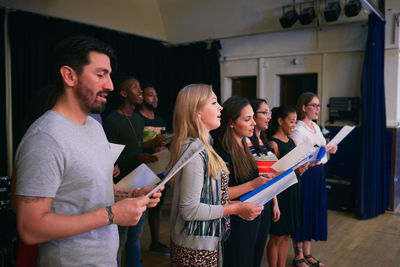 Male and female friends with music sheets singing at choir practice