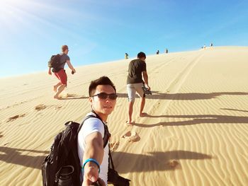 Friends standing on sand dune in desert against clear sky