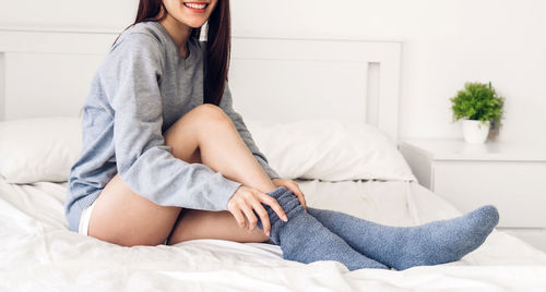 Midsection of woman sitting on bed at home