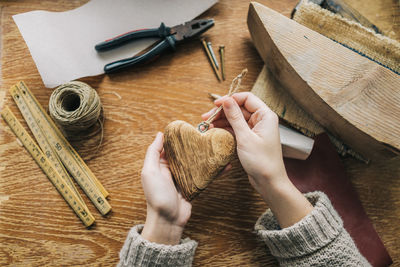 Cropped hands of woman holding wooden heart shape at table