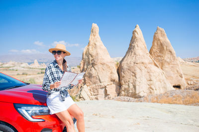 Side view of woman sitting on rock against sky