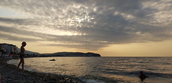 Woman standing on beach against sky during sunset