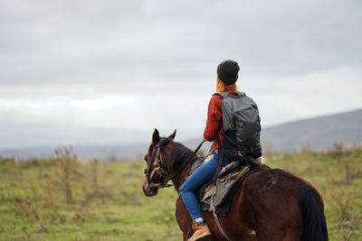 Rear view of man riding horse on field against sky