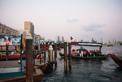 People sitting in boat by pier over sea against sky