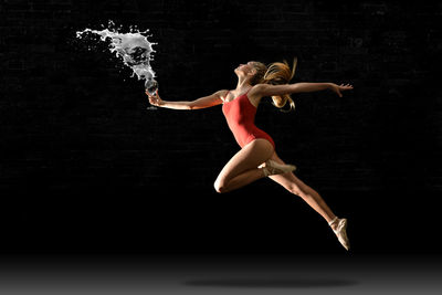 Full length of woman splashing drink while dancing against black background