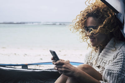 Mature woman using mobile phone at beach against sky