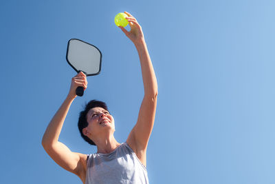 Low angle view of woman holding basketball hoop against clear blue sky