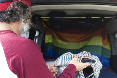 Rear view of a young man taking out the surfboard from the trunk of a car.