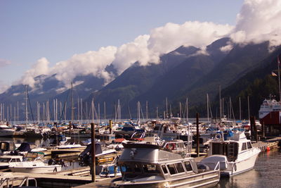 Boats moored at harbor against mountains and cloudy sky