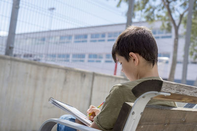 Teenage writing in book while sitting on bench