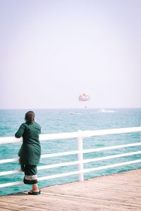 Rear view of woman standing by railing on bridge over see against clear sky