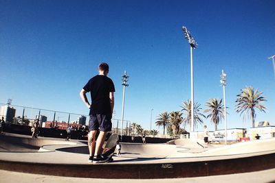 Rear view of skateboarder standing at skateboard park against clear sky