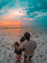 Rear view of man on beach against sky during sunset