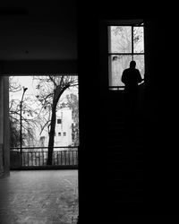 Rear view of silhouette man standing by window in building