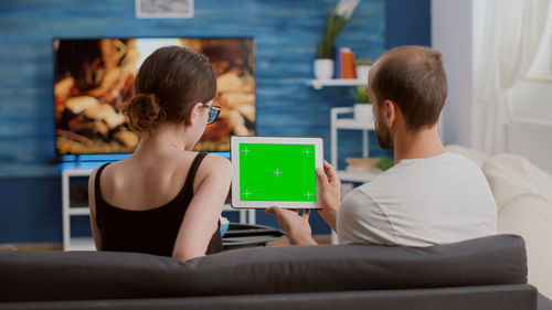 Rear view of man and woman using tablet pc at home