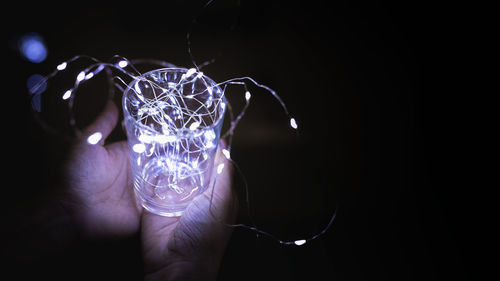 Close-up of hand holding illuminated glass against black background