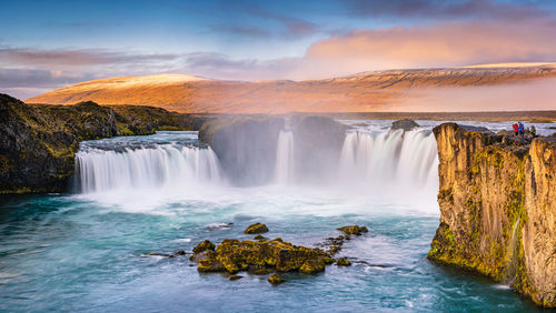 Scenic view of waterfall against sky during sunset