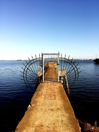 Pier on sea against clear blue sky