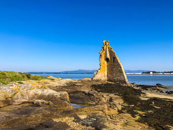 Rock on beach against clear blue sky