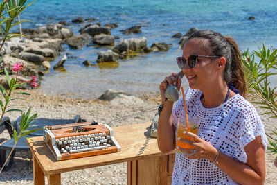 Young woman using telephone and holding drink at beach