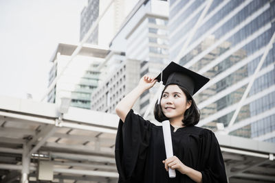 Young woman wearing black graduation gown standing in city