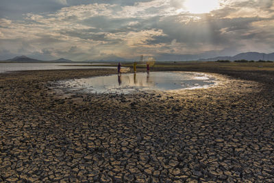 People fishing in pond by lake against sky