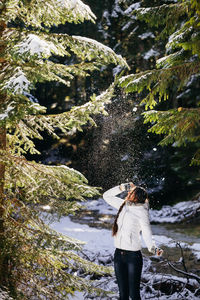 Young woman standing against river in forest during winter