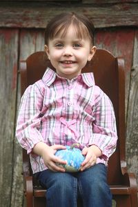 Portrait of smiling girl holding pumpkin while sitting on chair