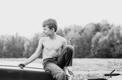 Full length of shirtless boy sitting against sky