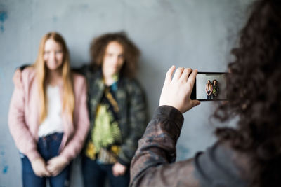 Teenage girl photographing friends standing against wall at parking garage