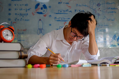 Young man studying with school supplies on table at home