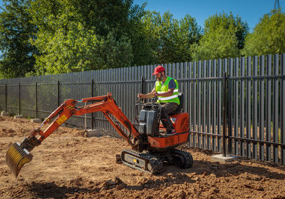 A man on a mini-excavator levels a piece of land, loosens the soil.