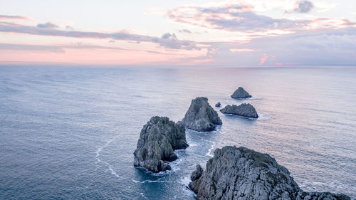 Rocks in sea against sky during sunset