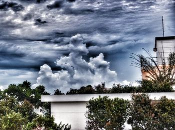 Low angle view of trees against cloudy sky