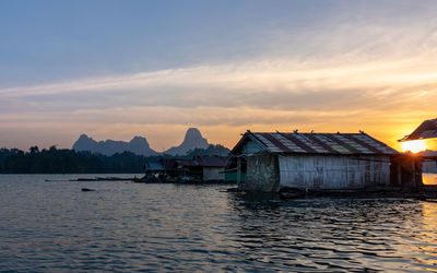 Houses by lake and buildings against sky during sunset