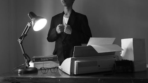 Midsection of businessman standing by book and lamp on table