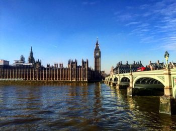 Big ben in front of river against blue sky in city