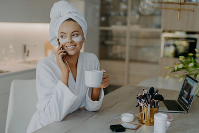 Smiling woman with eye patch talking on phone while holding coffee cup at home