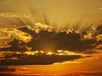 Low angle view of sunlight streaming through clouds during sunset