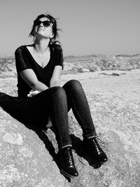 Full length of woman sitting on rock against clear sky