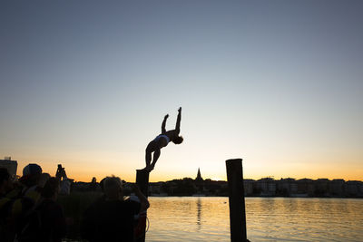 Silhouette people by river against clear sky during sunset