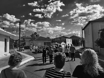 Rear view of people on street in city against sky