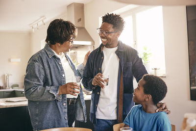 Senior woman with glass of water talking to son and grandson at home