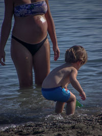 Rear view of shirtless girl with pregnant mother in sea