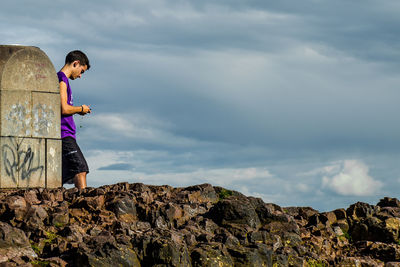 Side view of woman standing on rock against sky