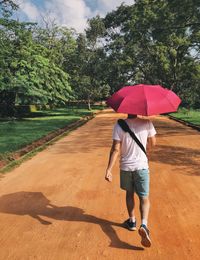 Rear view of man walking with umbrella on dirt road