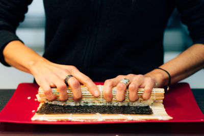Midsection of person rolling sushi in plate