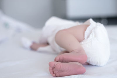 Low section of baby lying on bed at home